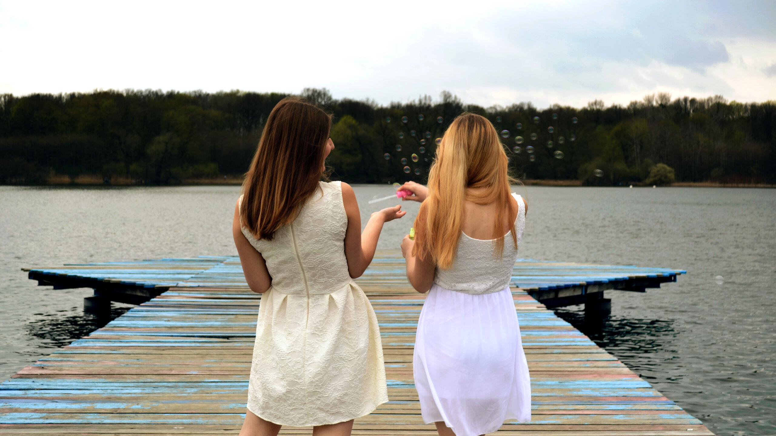 Dwie piękne dziewczyny w białych sukienkach puszczają bańki mydlane na pomoście