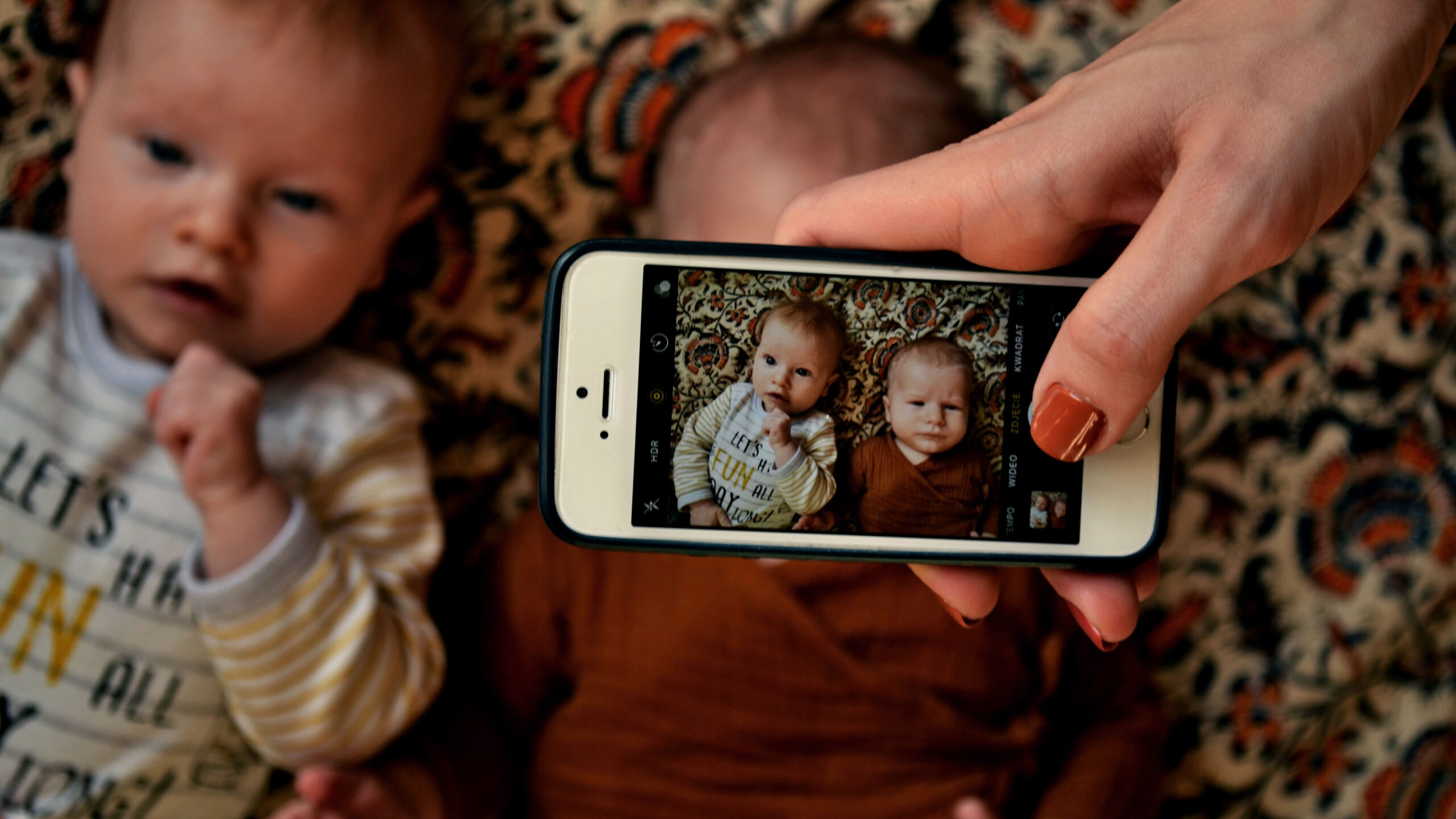 Zdjęcie dwóch niemowlaków, którym kobieta robi zdjęcie telefonem