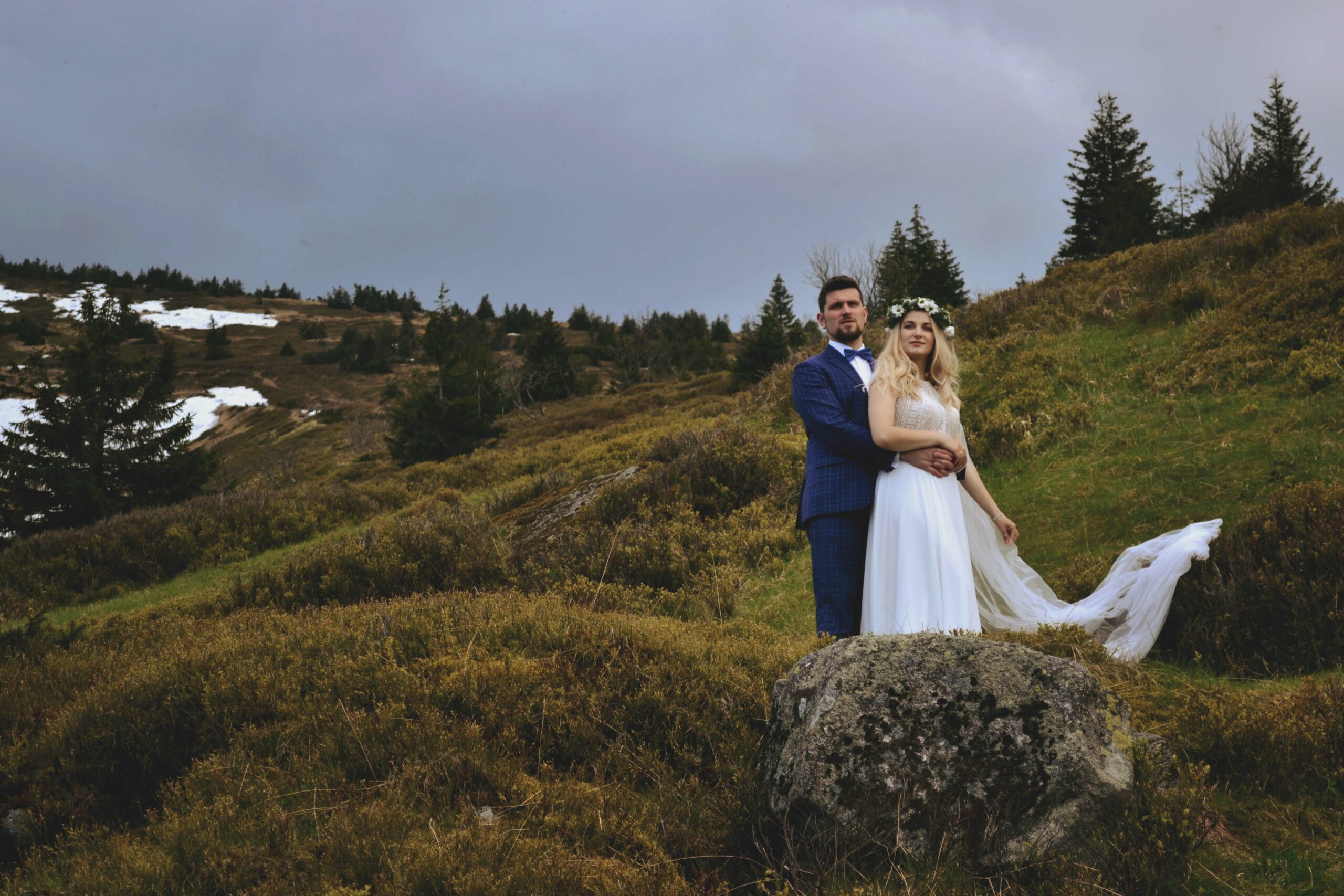 Ślubna sesja fotograficzna - młoda para stoi na kamieniu na tle gór